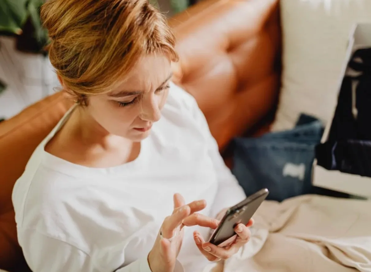 Persona utilizando un teléfono inteligente frente a una taza de café, analizando la hiperconexión digital
